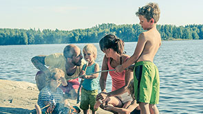 Eltern und vier Kinder machen ein Lagerfeuer am See.