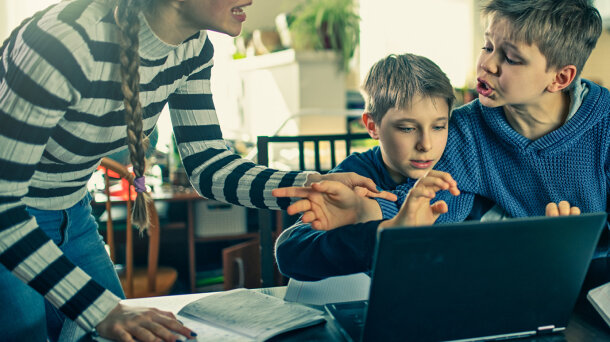 Zwei Jungen sitzen vor einem Laptop, eine Frau diskutiert mit ihnen.