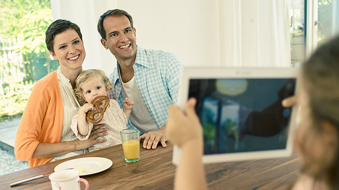 Familienszene: Kleines Mädchen fotografiert ihre Familie mit einem Tablet-Computer.