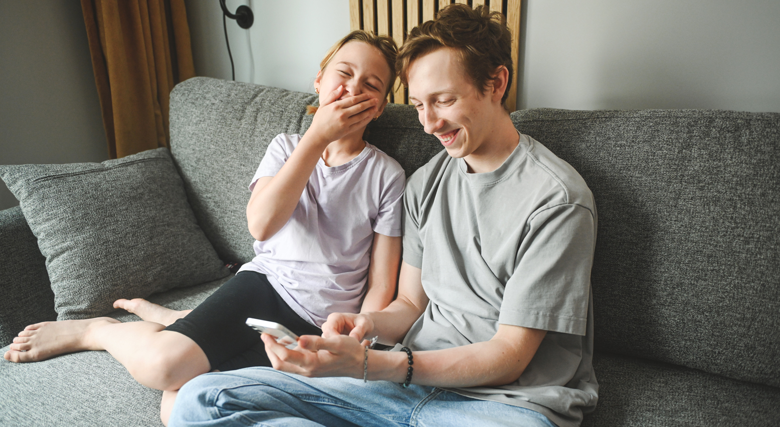 Teenager sitzen mit Handy nebeneinander und lachen